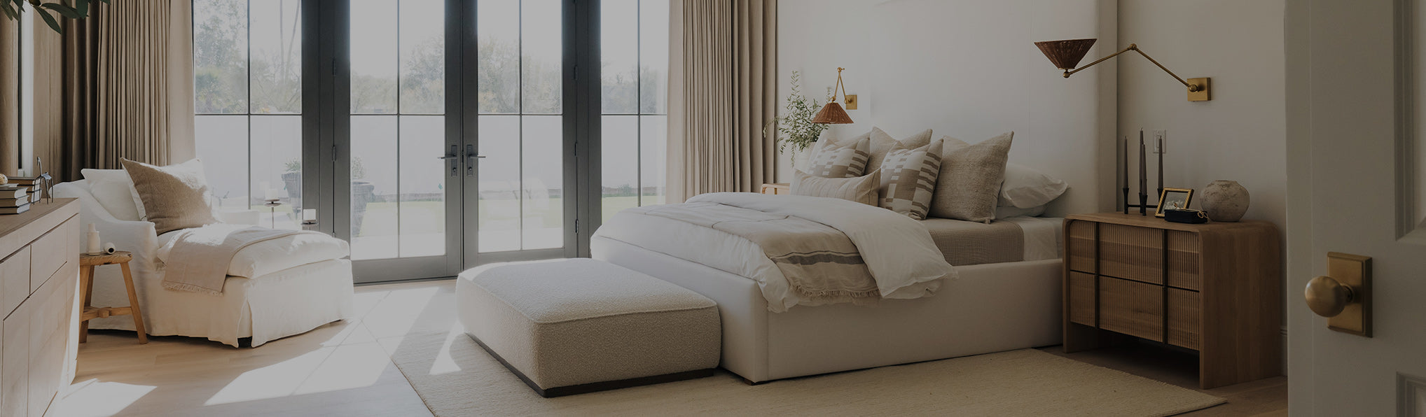 Light and airy bedroom with upholstered chair, ottoman, and bed in neutral colors and wood dresser