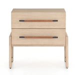 A light-finished oak nightstand with dual drawers featuring iron hardware wrapped in tan top-grain leather, with a clean silhouette and solid oak construction.