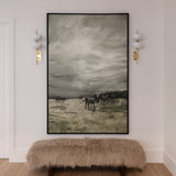 An oversized wall art depicting a horse, framed in black, mounted above a bench on a wall with two sconces.