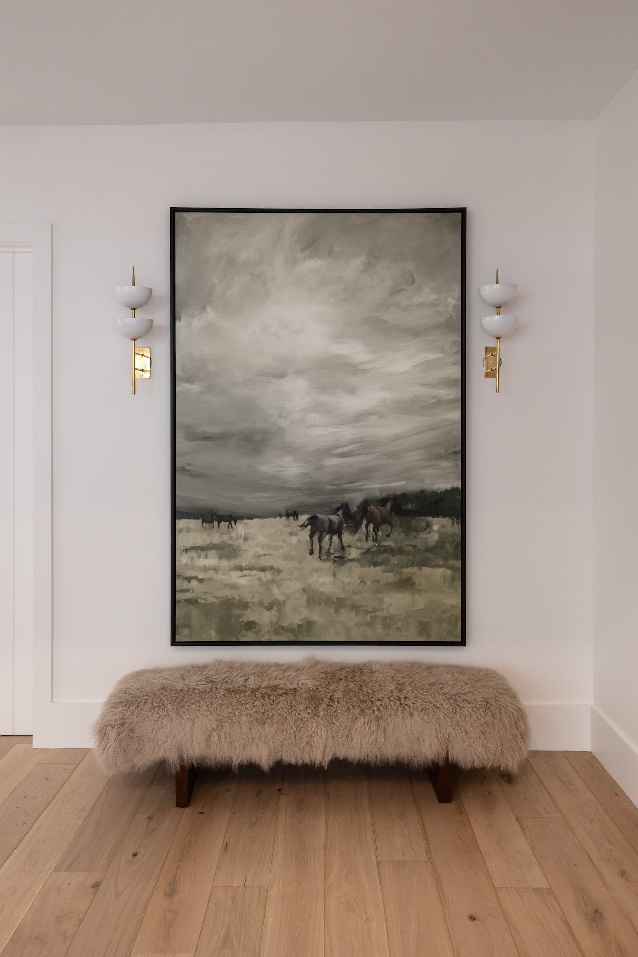 An oversized wall art depicting a horse, framed in black, mounted above a bench on a wall with two sconces.