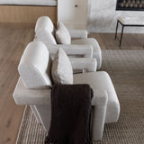 A row of modern light beige upholstered armchairs arranged on a woven Amity cream and gray area rug is ash wood in a contemporary living room, with a dark brown throw blanket draped over the front chair.