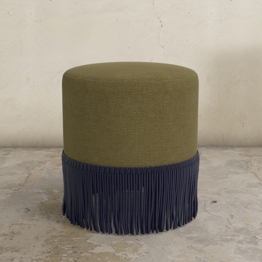 Green upholstered ottoman with  fringe on a concrete floor.