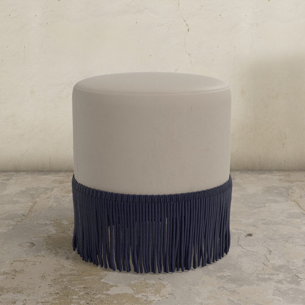 Round ottoman with navy blue fringe on a stone floor.