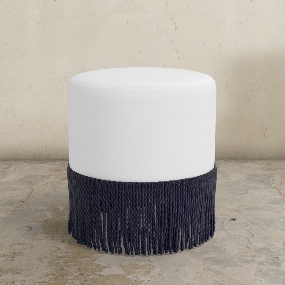 White upholstered ottoman with black fringes on a beige background