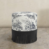 Round ottoman with black and white patterned top and black fringe on a beige background