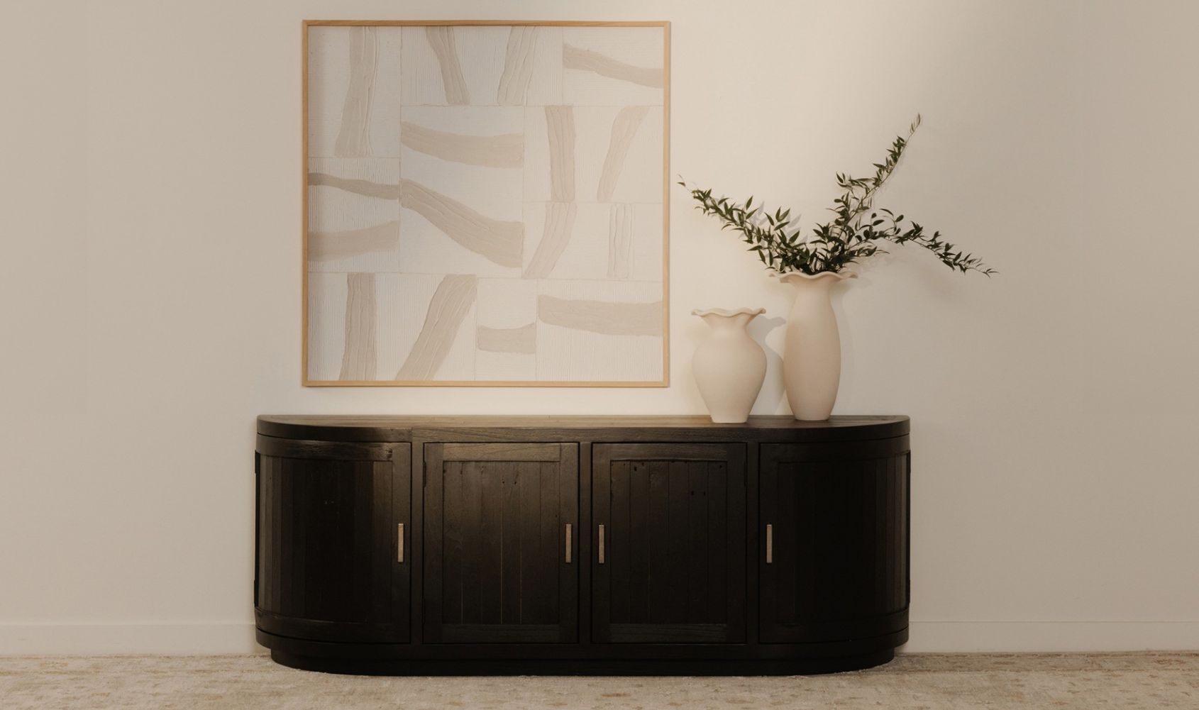 Nicola media tv cabinet against a wall with abstract art and a vase with greenery.