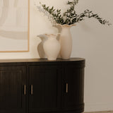 Dark wooden contemporary media console with two white vases and a lamp against a beige wall.