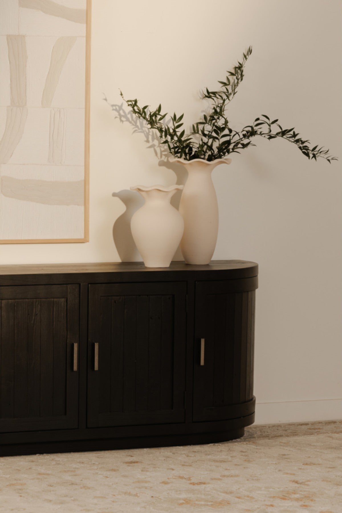 Dark wooden contemporary media console with two white vases and a lamp against a beige wall.