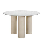 A round terrazzo concrete dining table with a pebble-polished top and fluted legs in a neutral color palette.