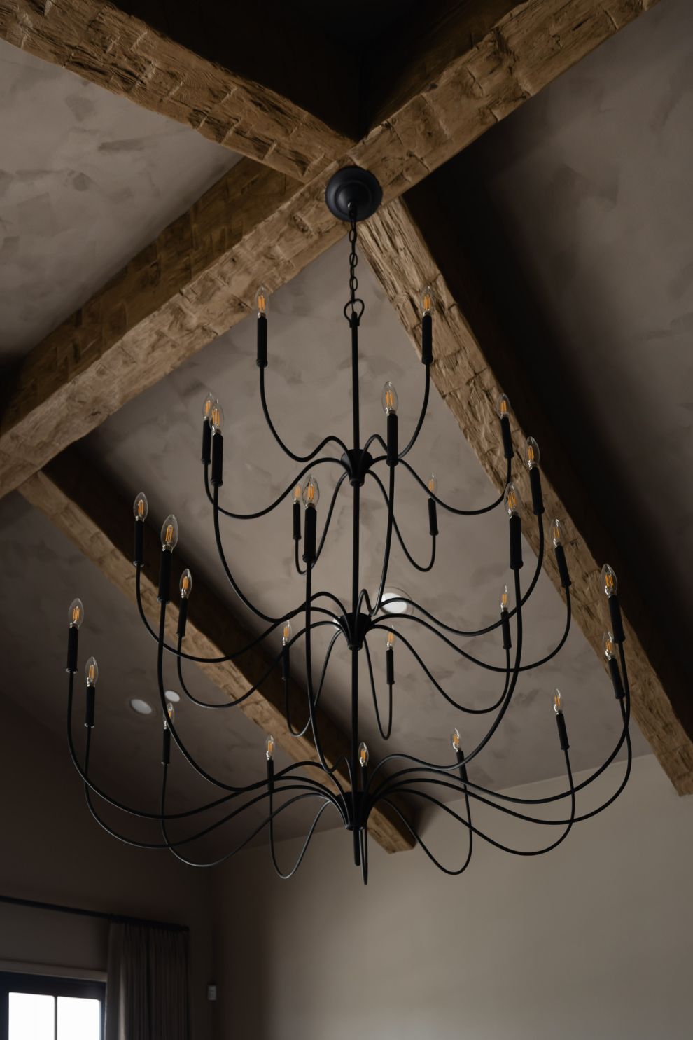 Tirrell Large Black candle style chandelier hanging from a ceiling with wooden beams