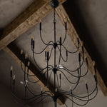 Tirrell Large Black candle style chandelier hanging from a ceiling with wooden beams