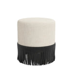 Round custom upholstered ottoman with beige cushion and black fringe on a white background