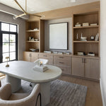 Modern home office with Regina Andrew Talon chandelier, wooden bookshelves, a white desk, and a large window.