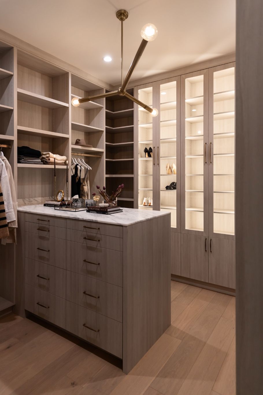 Modern walk-in closet with a Regina Andrew Talon modern chandelier shelves, drawers, and a central island.