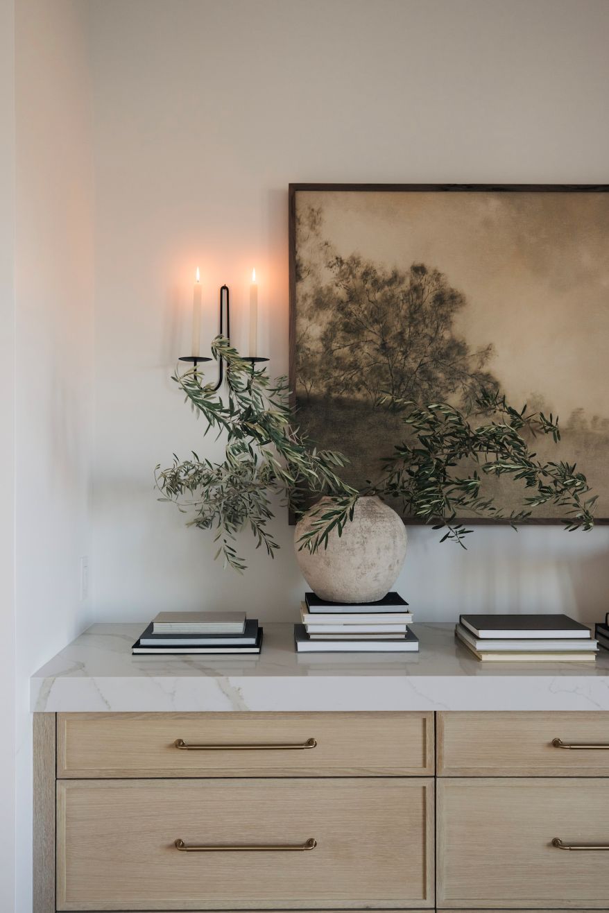 Decorative setup with a vase, books, and a framed landscape wall art on a white surface.