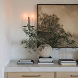 Decorative setup with a vase, books, and a framed landscape wall art on a white surface.