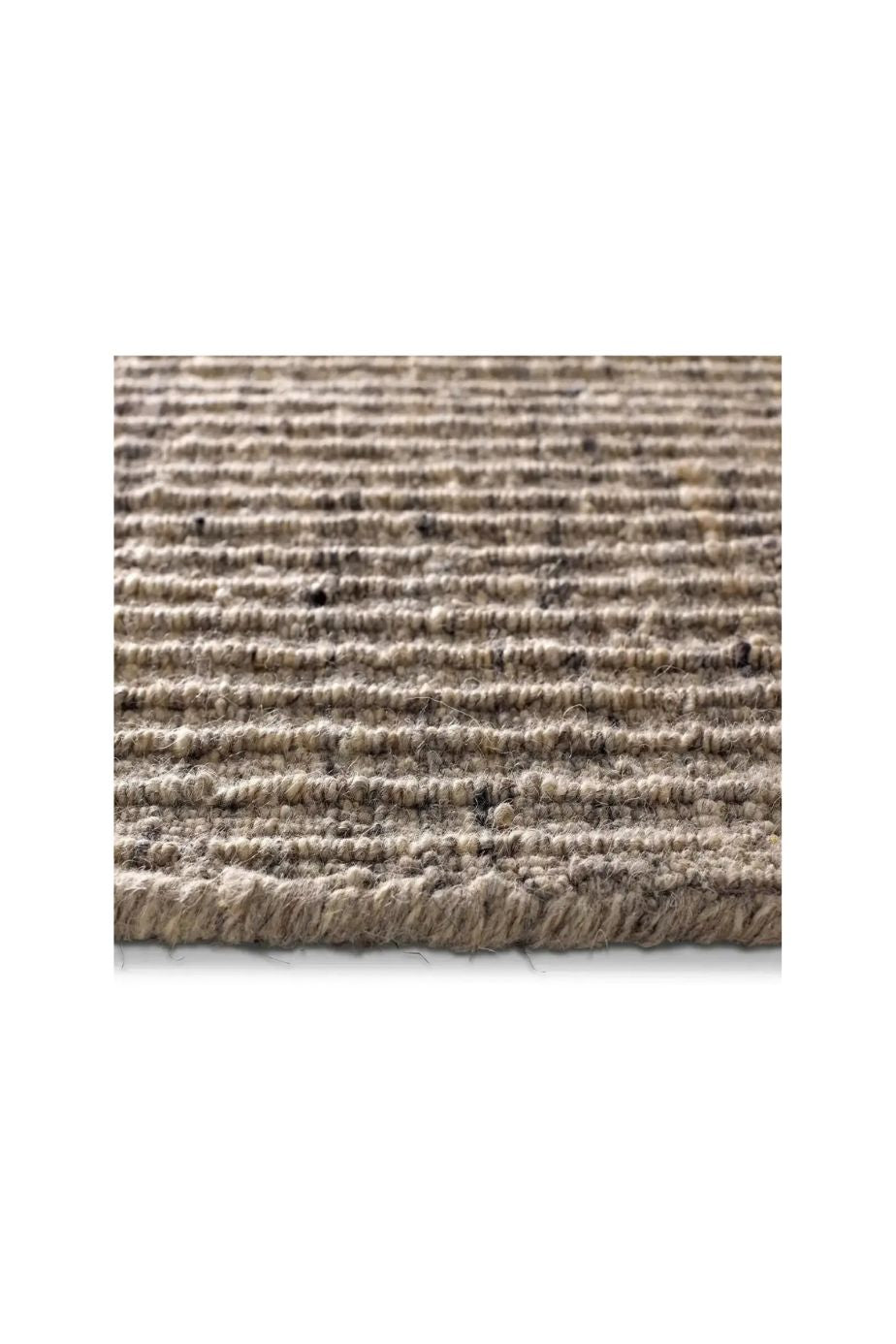 A close-up of a textured woven area rug or mat with horizontal ridges in a heathered beige and brown tone, shown against a white background.