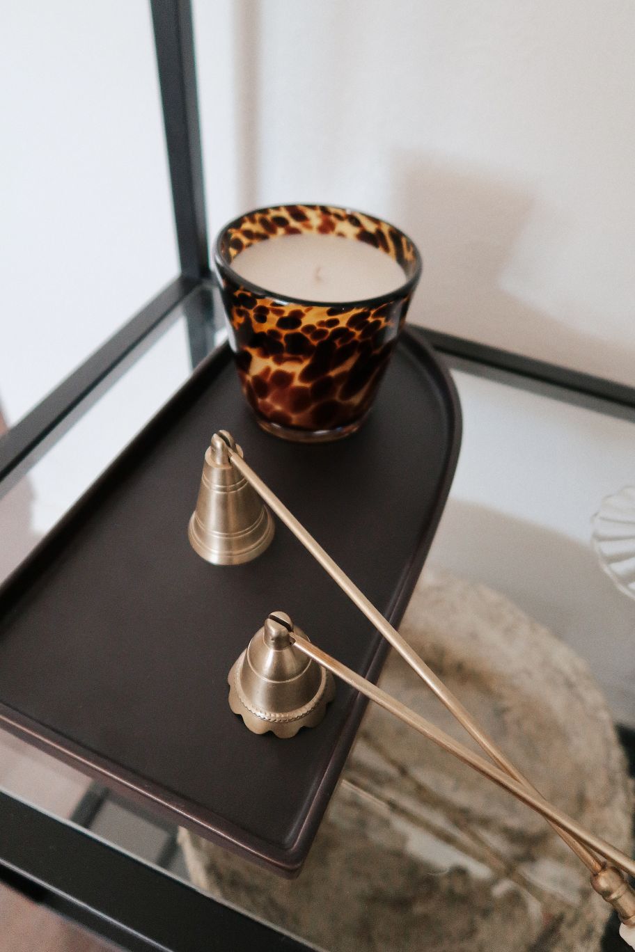 Scented candle with tortoise print holder on a dark surface next to decorative items.