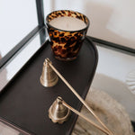 Scented candle with tortoise print holder on a dark surface next to decorative items.