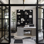 Modern office interior with a black bookshelf, unique white desk, and large glass doors.