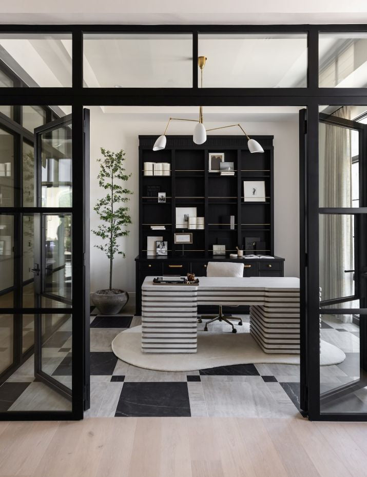 Modern office interior with a black bookshelf, unique white desk, and large glass doors.